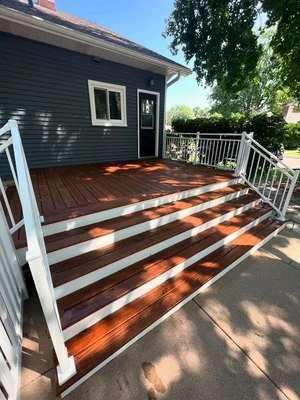 Dark siding house with white-trimmed porch, white railings, and stained wood deck with two-tone finish