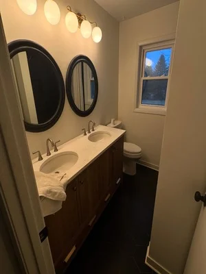 Bathroom with freshly painted walls, dark vanity, dual round mirrors, and updated lighting fixtures